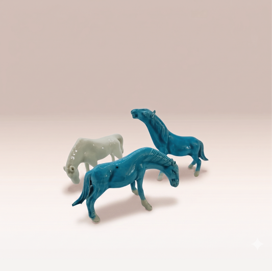 Ensemble de trois chevaux en porcelaine aux teintes turquoise et blanc nacré. Deux ont la tête baissé et l'un à la tête vers le haut.