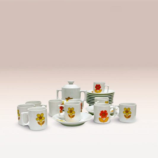 Ensemble de tasse, sous-tasse et cafetière vintage avec deux poignets sur les côtés. Des fleurs décorent tous éléments de l'ensemble.