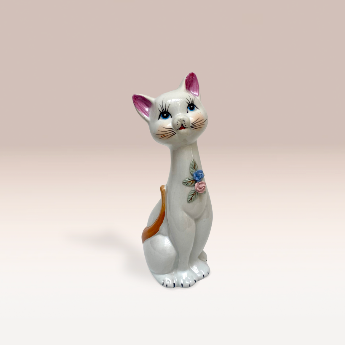 Statuette de chat en porcelaine avec des fleurs sur son cou.