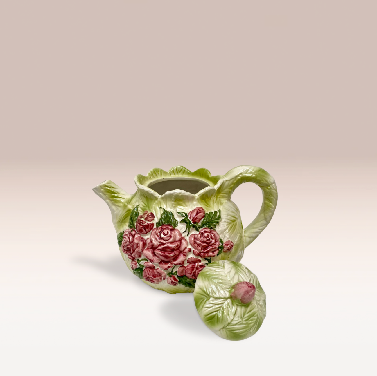 Théière en barbotine de couleur vert clair et texture feuille de chou. Des roses ornent les deux faces de la théière de forme ronde. Un poignet et un couvercle sont avec.